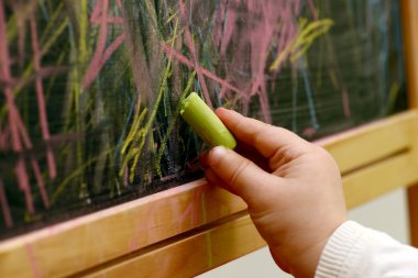child draws with chalk on a blackboard clipart