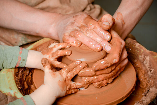 A potters hands guiding pupil hands to help him to work with the ceramic wheel