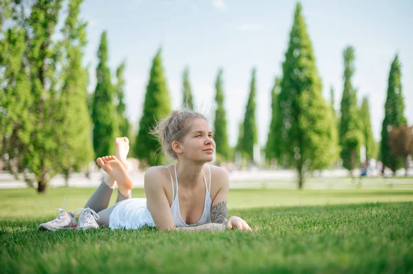 Atractiva chica deportiva se encuentra en la hierba y se relaja en el parque — Foto de Stock