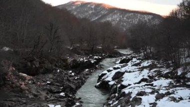 Gün batımında karlı dağ nehri. Yeşil renkli su.