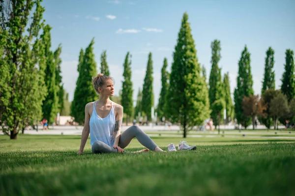 Приваблива спортивна дівчина лежить на траві і відпочиває в парку Стокове Зображення