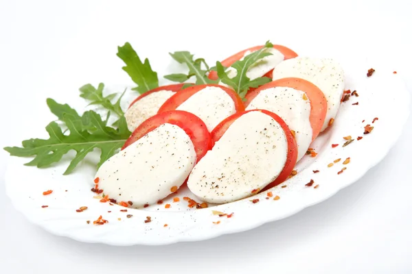 Tomate y mozzarella con hojas de albahaca en un plato — Foto de Stock