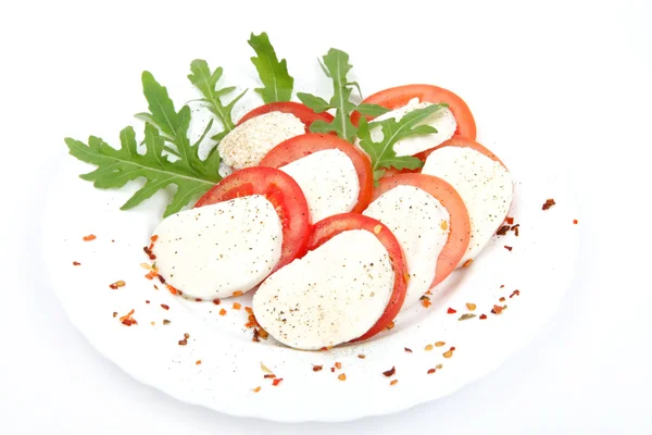 Tomaten und Mozzarella mit Basilikumblättern auf einem Teller — Stockfoto