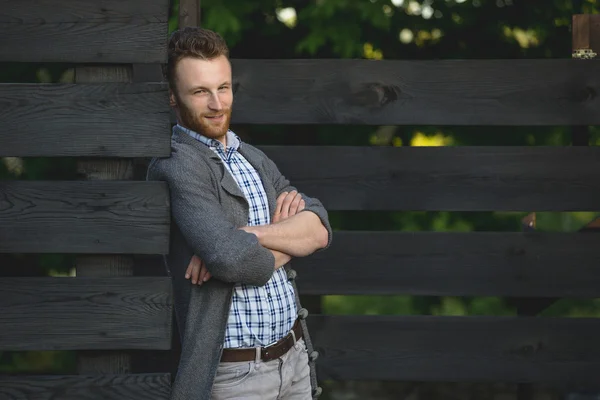 Portrait of young fashionable man against wooden fence — Stock Photo, Image