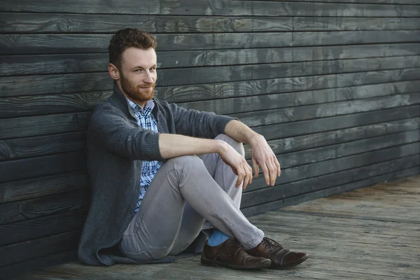 Красивый молодой человек, сидящий на деревянном полу — стоковое фото