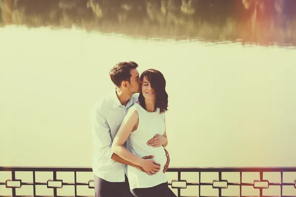 Glückliches und junges schwangeres Paar, das sich in der Natur am See umarmt. v — Stockfoto