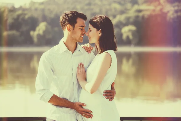 Feliz y joven pareja embarazada abrazándose en la naturaleza en el lago. V. —  Fotos de Stock