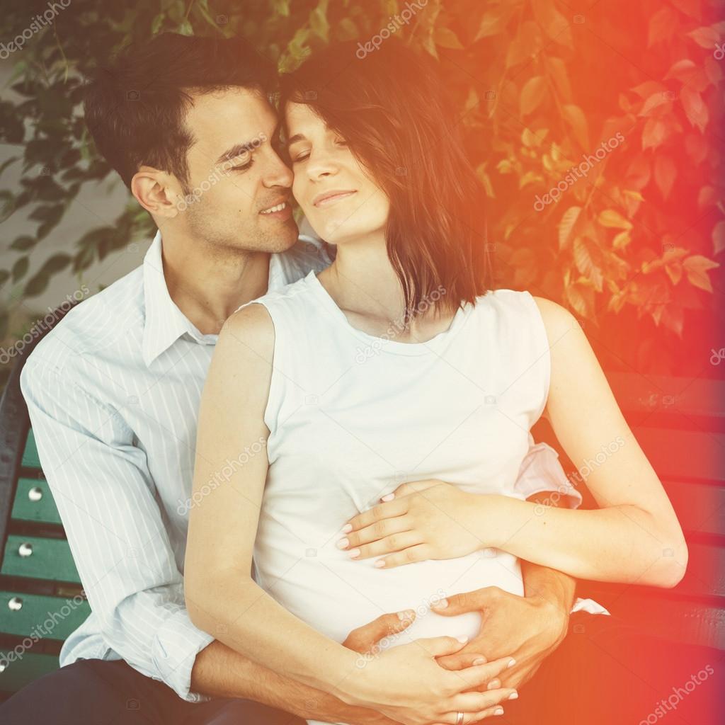 Happy and young pregnant couple hugging in nature. Vintage retro