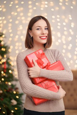 Güzel esmer kadın dekore edilmiş oturma odasında bir yığın hediye kutusu tutuyor.