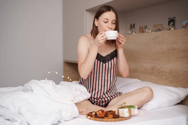 Γυναίκα πίνουν καφέ στο κρεβάτι με δώρα — Φωτογραφία Αρχείου