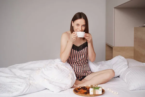 Wanita minum kopi di tempat tidur dengan mempersembahkan — Stok Foto