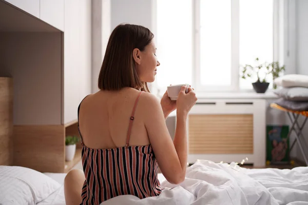 Kobieta pije rano kawę w łóżku. — Zdjęcie stockowe