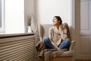 Zeki modaya uygun giyinmiş gülümseyen bayan koltukta oturuyor. Gülümsemek, evde rahat bir atmosferde oturmak, güzel tasarım. Rahat ve rahat kız zamanı