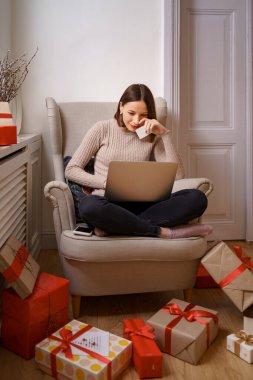 Genç bir kadın kredi kartı ve dizüstü bilgisayarla online alışveriş yapıyor.