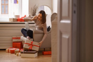 Evdeki koltukta oturan bir kadın dizüstü bilgisayarla çalışıyor, cep telefonuyla konuşuyor.