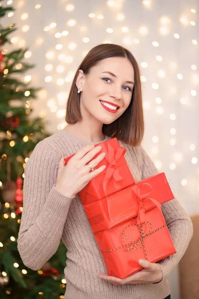 Hermosa mujer morena sosteniendo montón de cajas de regalo en la sala de estar decorada — Foto de Stock