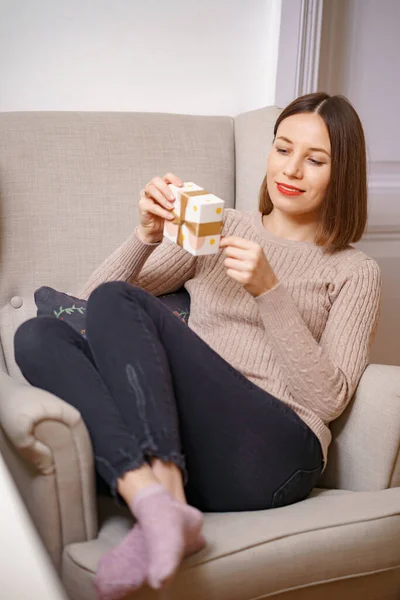 Vrouw in een fauteuil thuis met een cadeautje in haar hand — Stockfoto