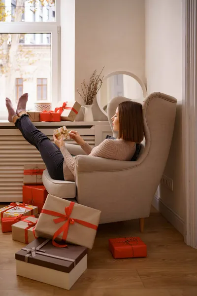 Egy nő ül otthon egy karosszékben, ajándékkal a kezében. — Stock Fotó