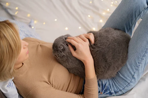 Mujer joven y gato en la cama en la habitación —  Fotos de Stock