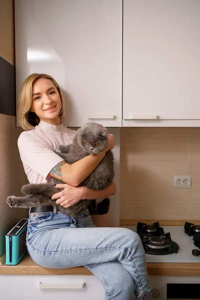 Женщина, сидящая на кухне и обнимающая кота — стоковое фото