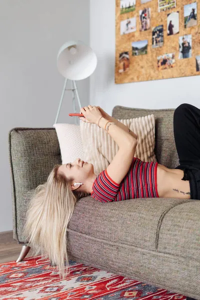 Mujer joven escuchando música tumbado sofá en casa usando el teléfono — Foto de Stock