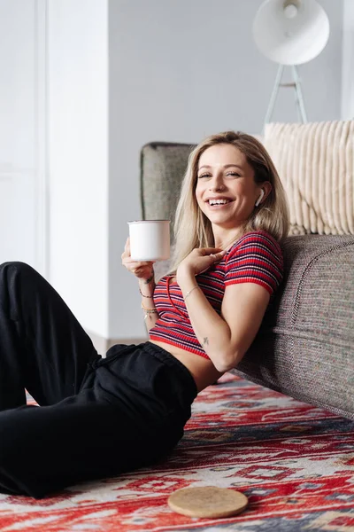Ung kvinna lyssnar musik sitter nära soffan hemma — Stockfoto