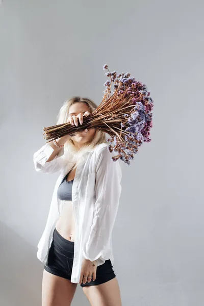 Jeune femme en chemise blanche posant avec un bouquet de fleurs — Photo