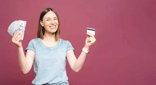 Excited woman holding money and credit card isolated over pink crimson background — Stock Photo, Image