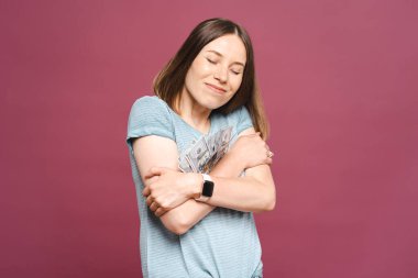 Mutlu kadın pembe arka planda dolarları kucaklıyor