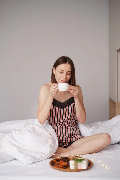 女性はプレゼントとベッドの中でコーヒーを飲む — ストック写真