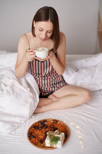 Egy nő kávét iszik az ágyban ajándékokkal. — Stock Fotó
