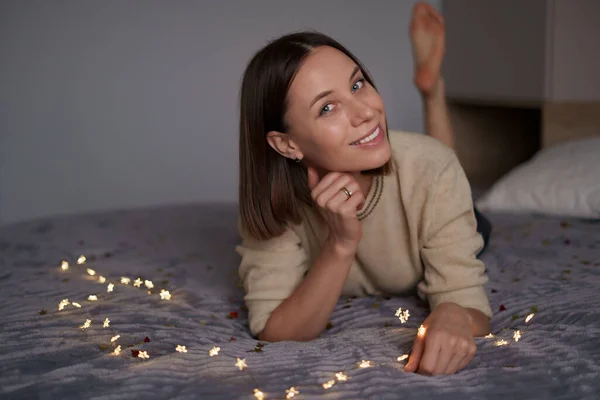 Прекрасная женщина лежит на кровати с сияющими огнями — стоковое фото