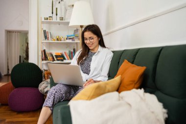 İş kadını dizüstü bilgisayarla çalışıyor evde oturuyor ve işlerini ev ofisinden yönetiyor.