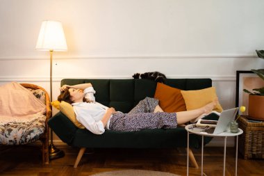 Evdeki kanepede uzanan genç kadın dinleniyor.