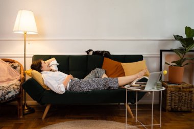 Evdeki kanepede uzanan genç kadın dinleniyor.