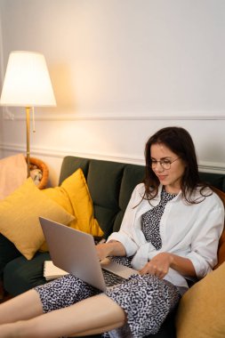 İş kadını dizüstü bilgisayarla çalışıyor evde oturuyor ve işlerini ev ofisinden yönetiyor.