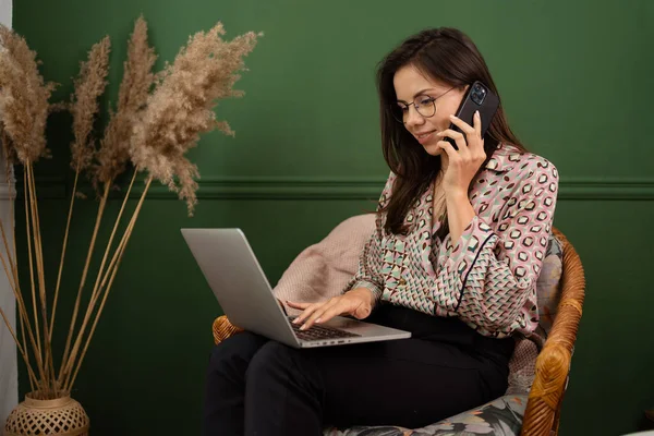 Весела молода красива жінка розмовляє по телефону і використовує ноутбук — стокове фото