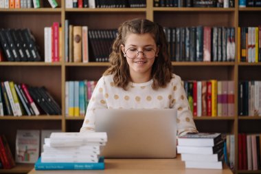 Girl studying among books using laptop