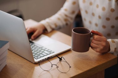 Woman working on a laptop holding a cup