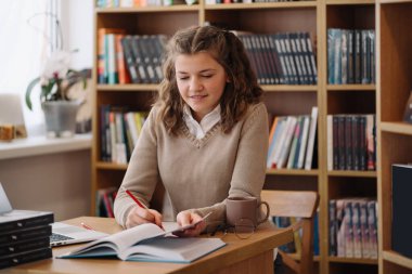 Girl studying among books sitting at the desk among books