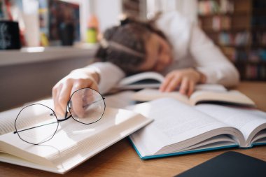 Tired student got asleep on the desk while studying among books