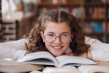 Girl studying among books sitting at the desk among books