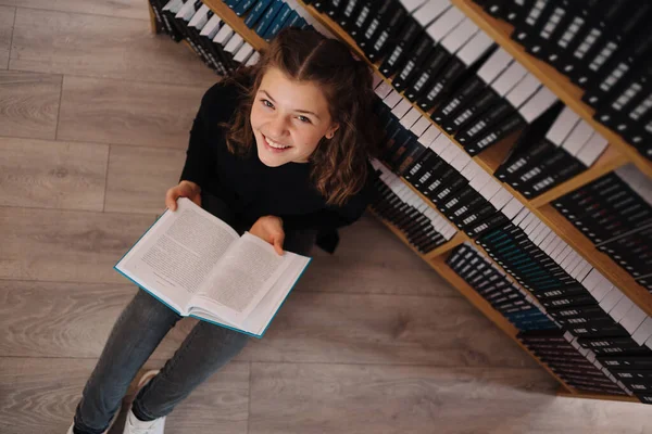 Девочка учится читать книгу, сидя на полу среди книг в книжном магазине — стоковое фото