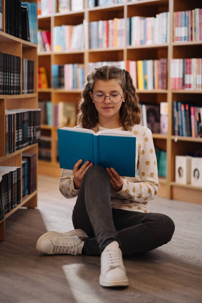 Beautiful girl is studying reading a book while standing on the floor among books in the bookshop