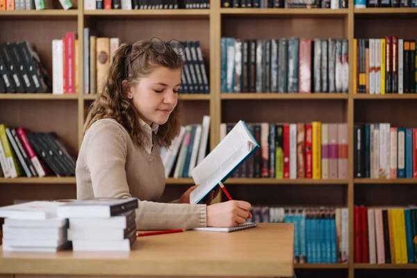 Girl studying among books sitting at the desk among books — Stok fotoğraf