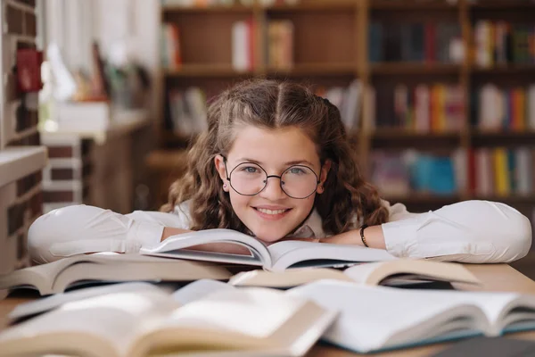 Girl studying among books sitting at the desk among books — Stockfoto