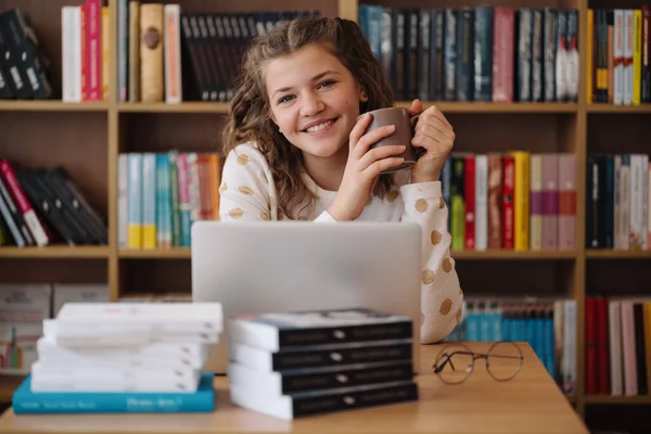 Girl studying among books using laptop ストック写真