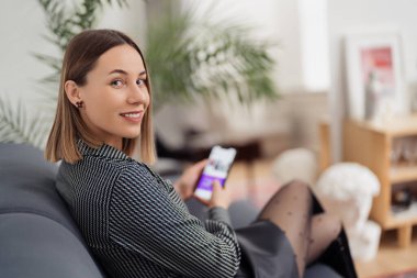 Kanepede otururken telefonu elinde tutan kadın.