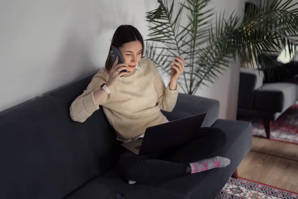 Жінка використовує ноутбук під час розмови по телефону у вітальні — стокове фото