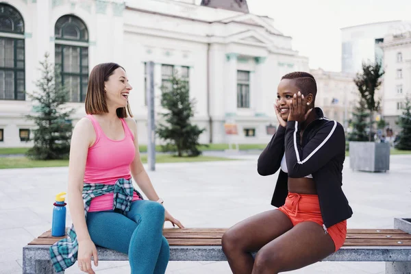 Two multiethnic curvy girls relaxing after exercise session, outdoor communicating. — Stock Photo, Image